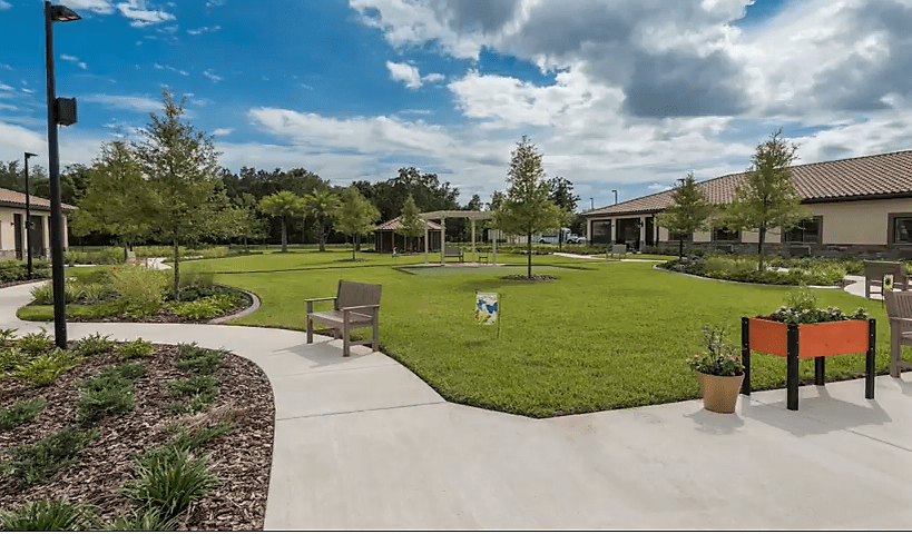 A scenic view of a landscaped garden with a pathway, benches, and lush greenery under a partly cloudy sky.
