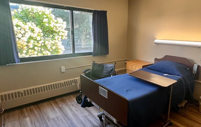 A hospital room with a bed, wheelchair, and window with curtains.