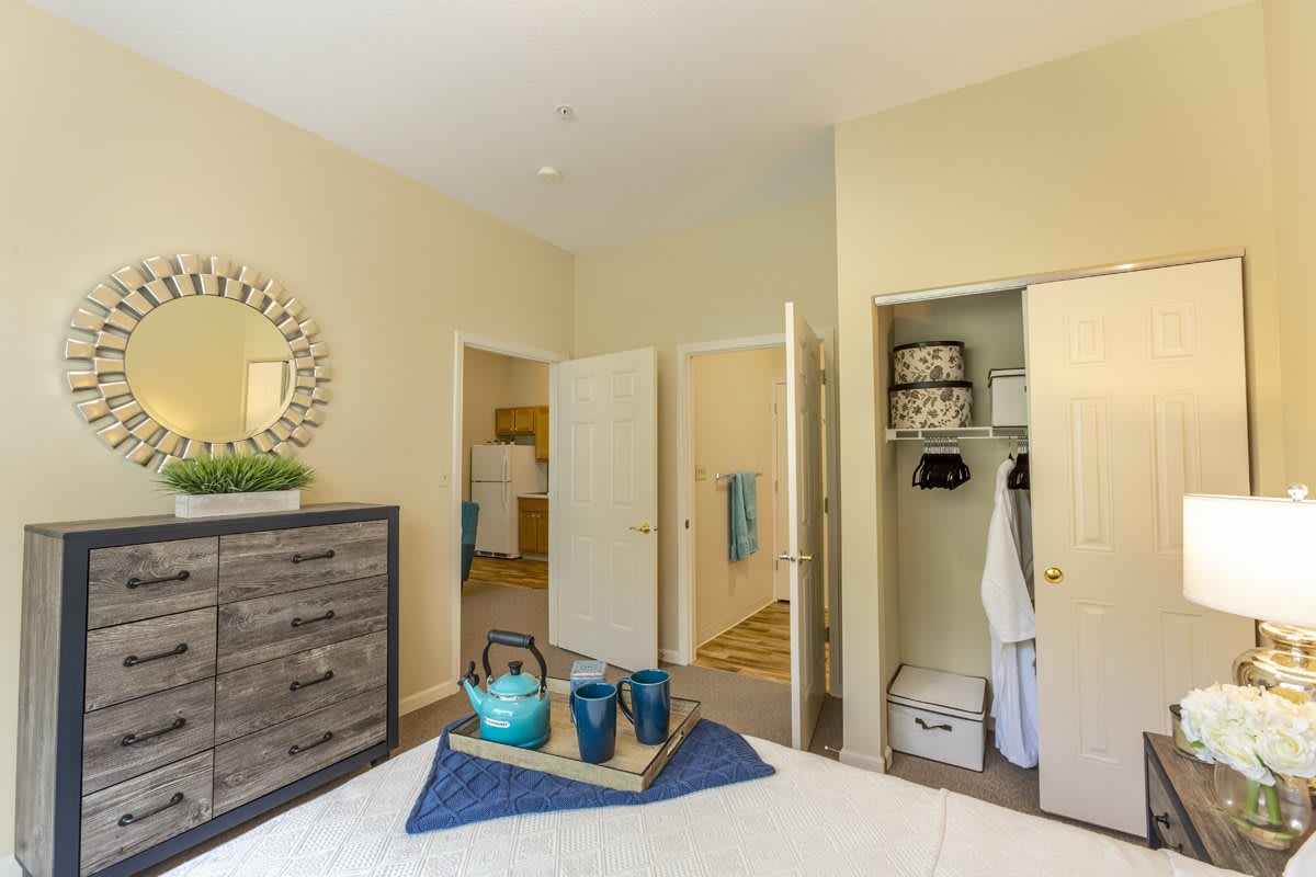 A cozy bedroom with beige walls, a neatly arranged dresser, and an open closet.