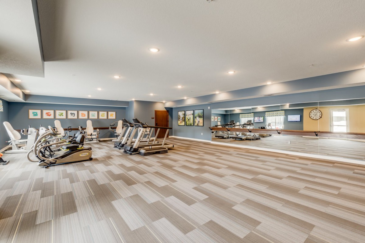 A spacious gym with modern exercise equipment and large mirrors.