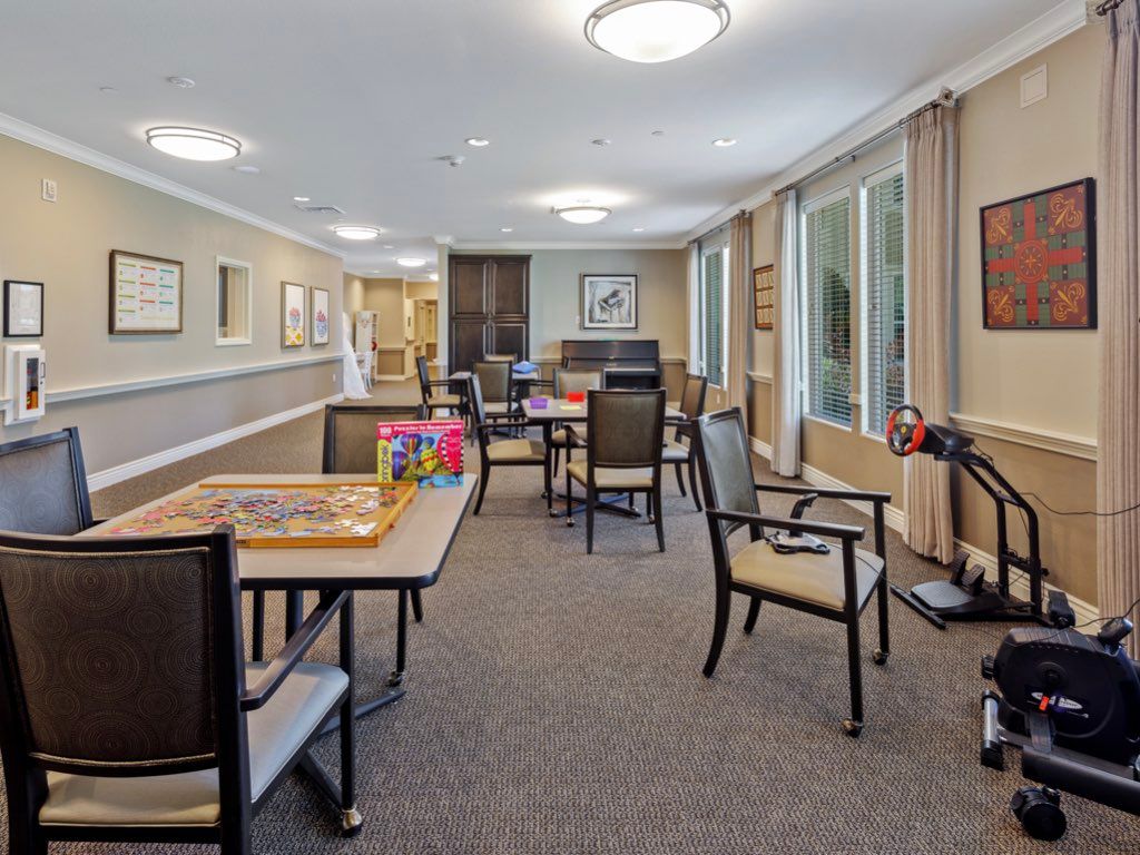 A spacious community room featuring tables and chairs, with board games set out and large windows providing natural light.