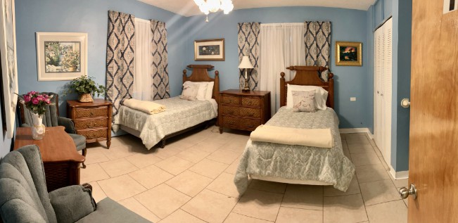 A cozy bedroom with two neatly made twin beds, a wooden dresser, and elegant curtains.