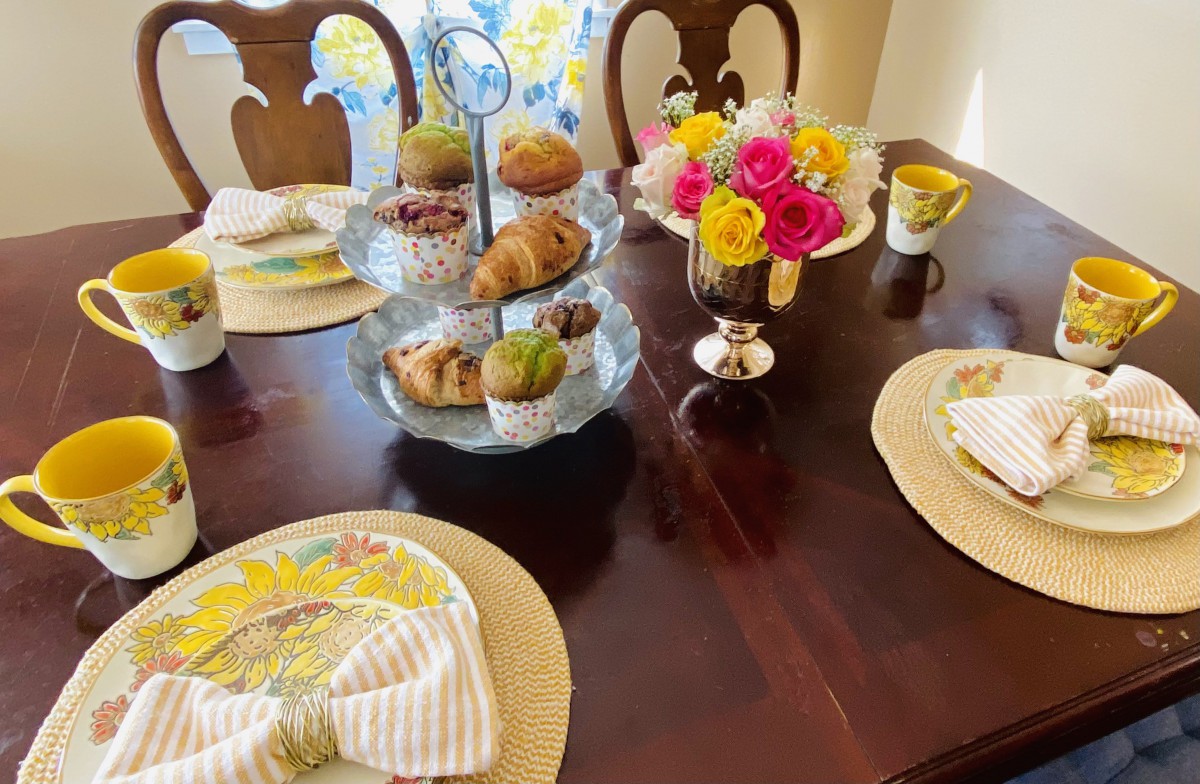 A beautifully set breakfast table with muffins, a tiered stand, floral centerpiece, and tea cups.