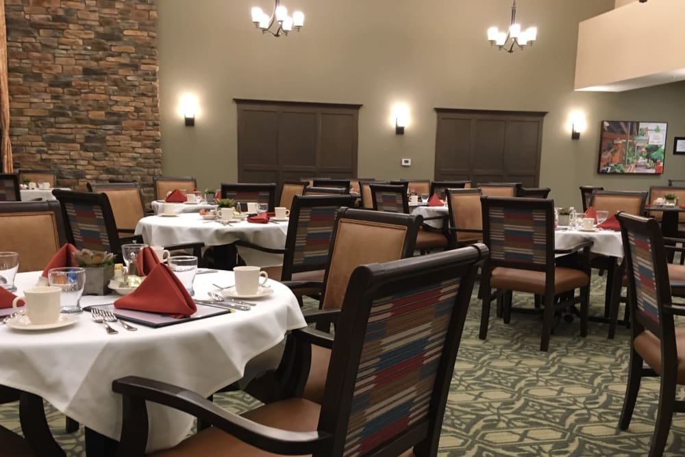 A neatly arranged dining room with tables set for guests, featuring comfortable chairs and elegant lighting.