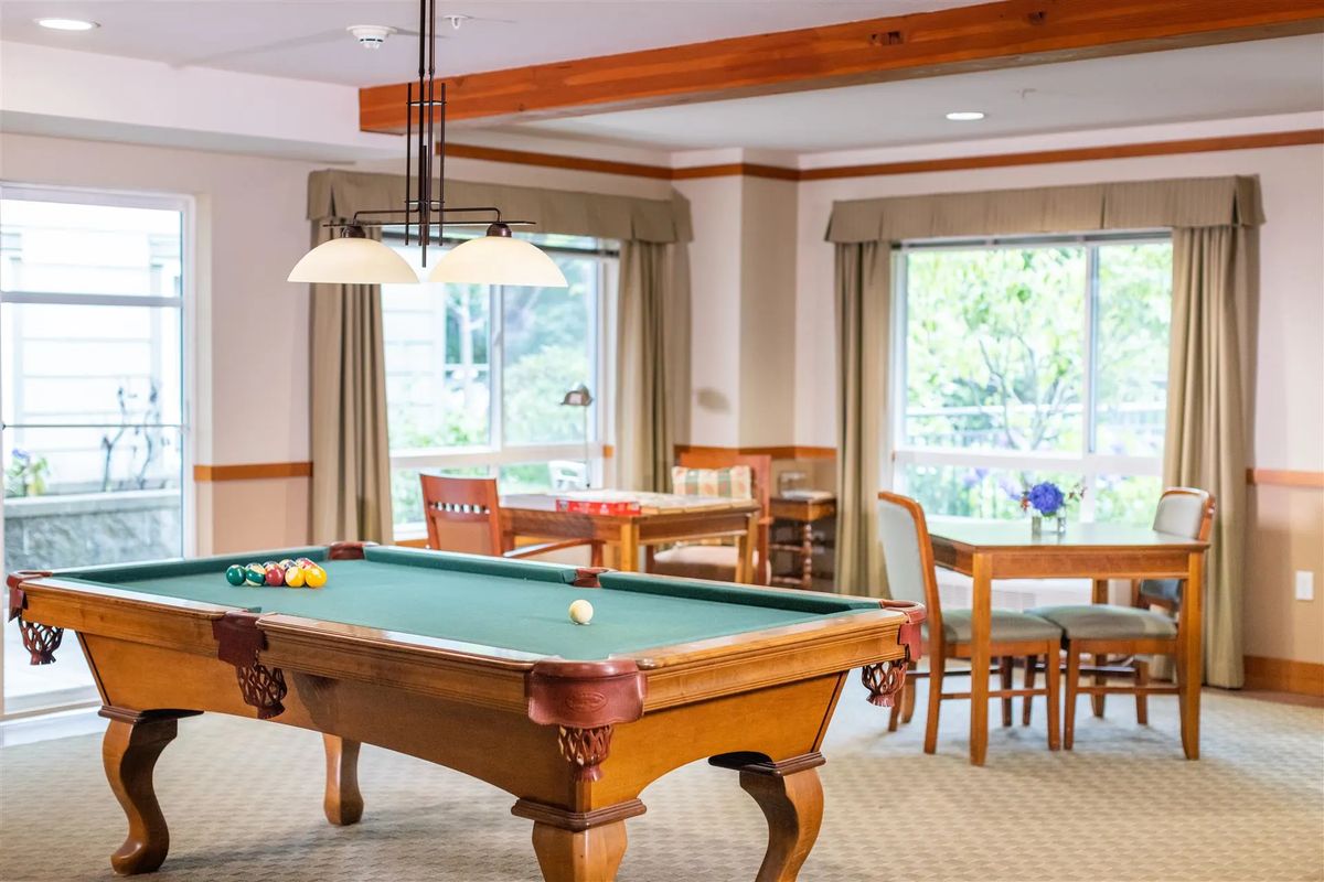A well-lit game room featuring a pool table and cozy seating area by the windows.