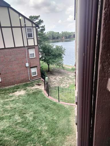 A view from an apartment window overlooking a serene lake and green lawn.
