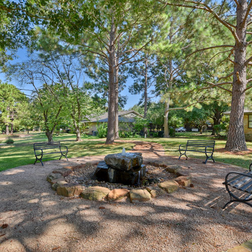 A serene park setting with a central fountain surrounded by benches and lush trees.