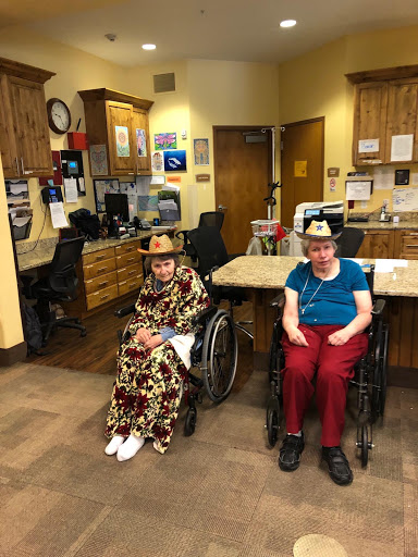 Two residents of a care home enjoying their time together, each in a wheelchair and dressed in vibrant clothing.