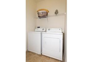 A compact laundry room with a washing machine and dryer, featuring a shelf with a laundry basket.