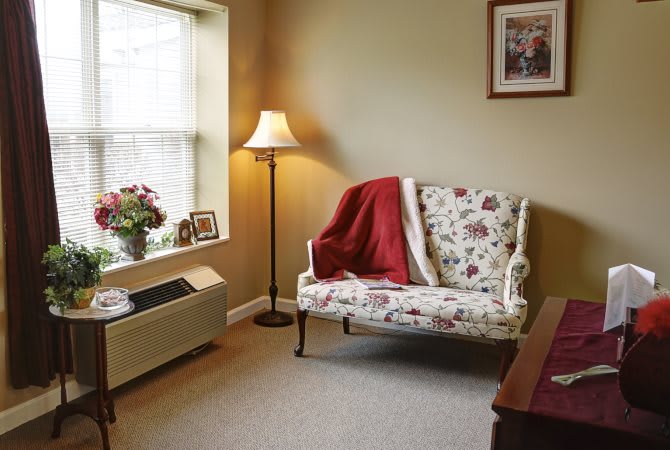 A cozy living room with a floral-patterned couch, floor lamp, and window view.