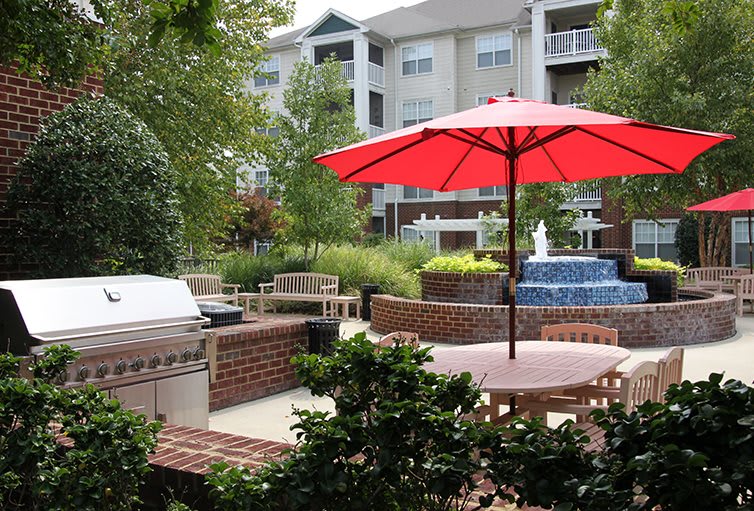 A peaceful outdoor patio with seating, a red umbrella, and a fountain at an apartment complex.