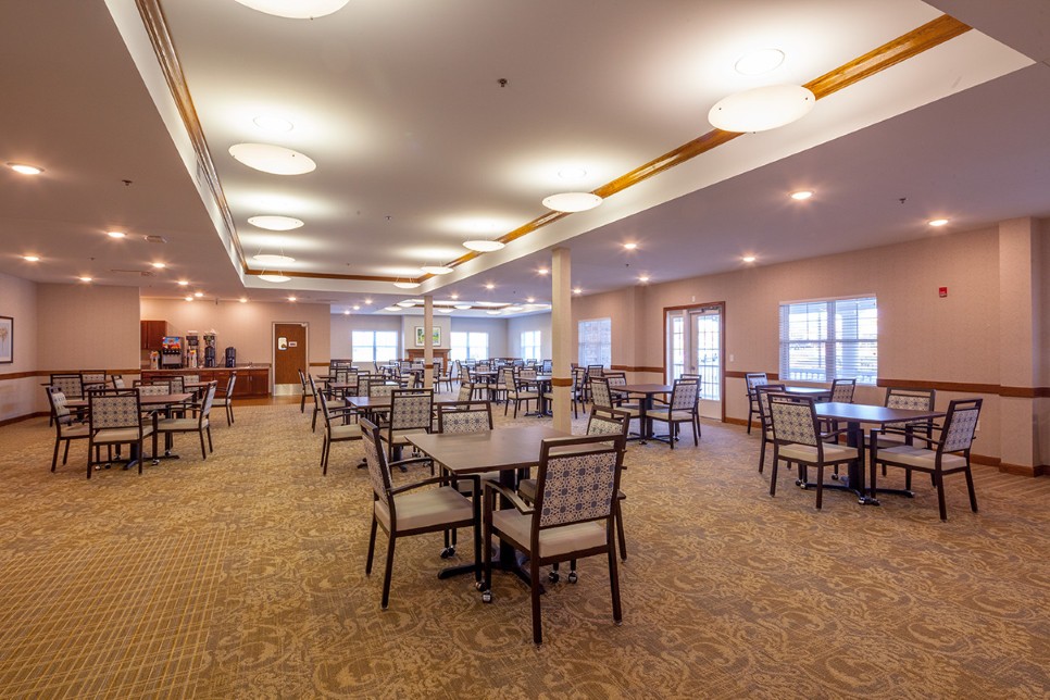 A spacious dining area with multiple tables and chairs, well-lit and featuring a carpeted floor.