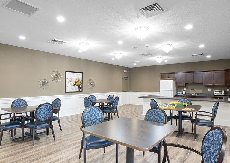 A modern dining area with tables, chairs, and a small kitchen in the background.