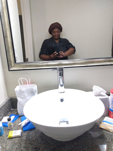 A person taking a selfie in a bathroom mirror surrounded by various toiletries.