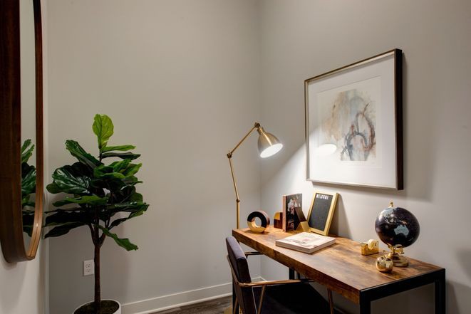 A minimalist home office with a wooden desk, framed artwork, and a potted plant.