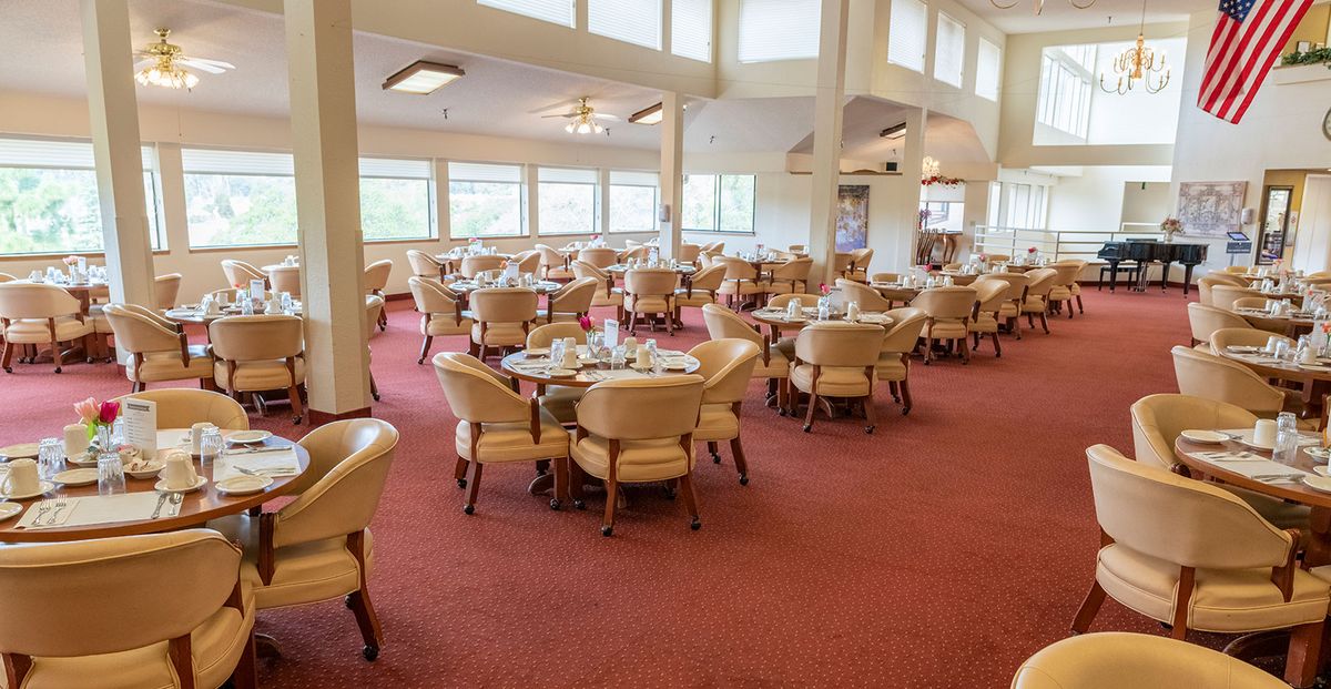 An elegant restaurant dining area with neatly arranged tables and chairs, featuring large windows and a carpeted floor.