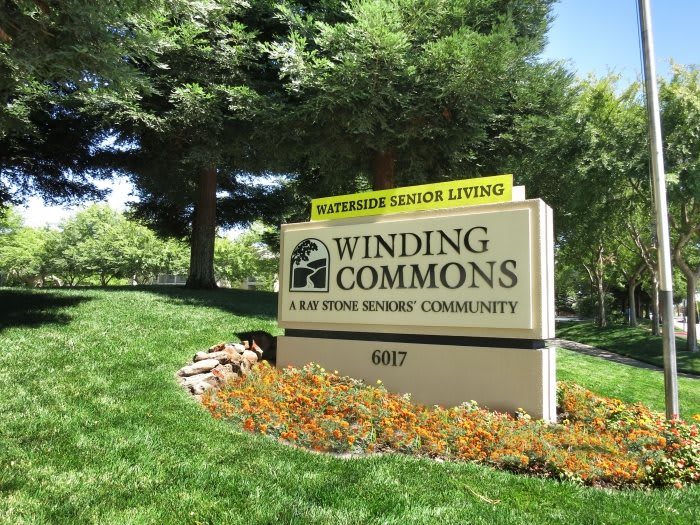 Sign for Winding Commons, an assisted senior living community, surrounded by well-maintained landscaping and trees.