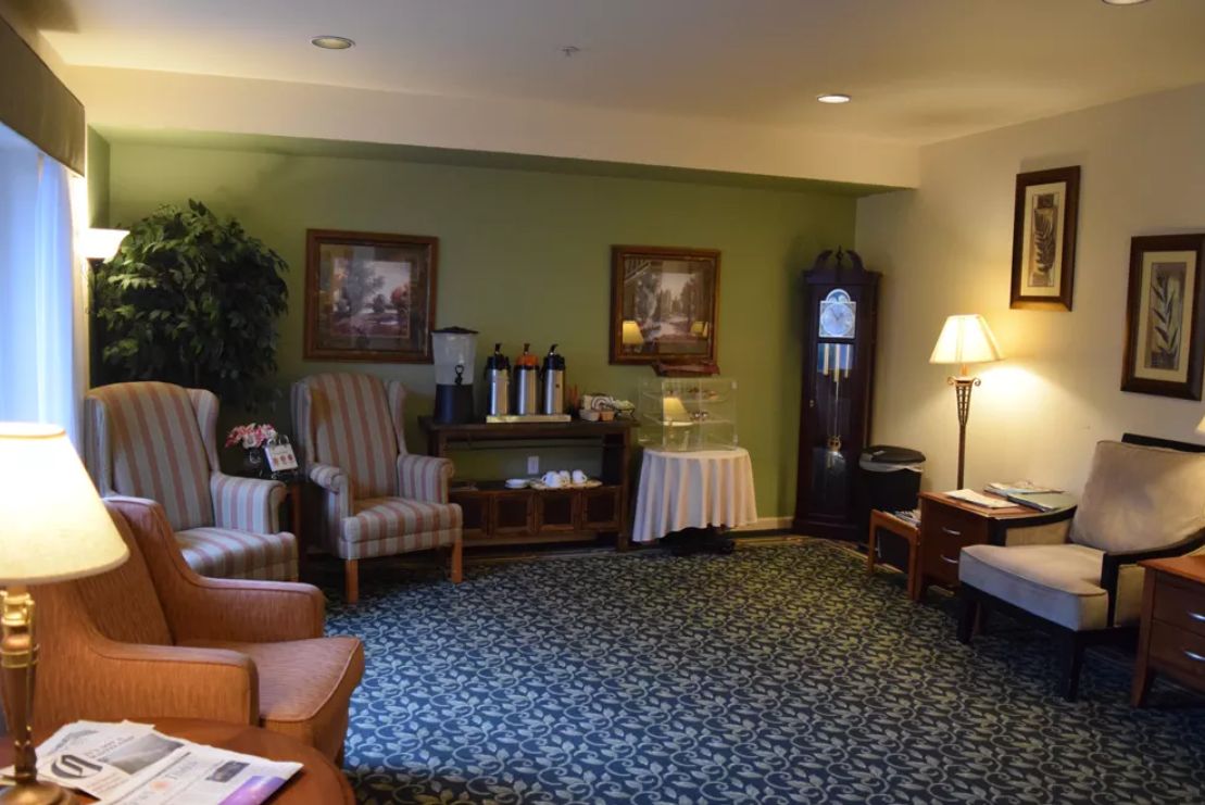 A cozy lobby area featuring armchairs, a table with a lamp, wall art, and a grandfather clock.