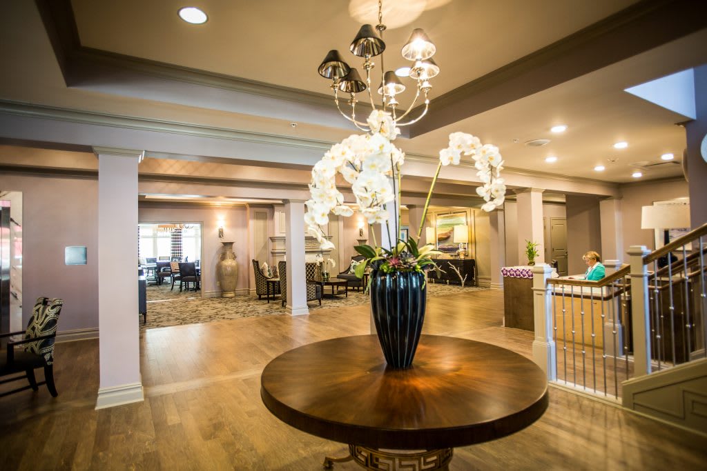 A modern lobby interior featuring a central table with an elegant flower arrangement and chandelier lighting.