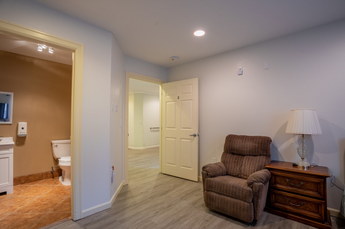 A cozy living room with a comfortable recliner and wooden flooring, featuring an open doorway to another room.