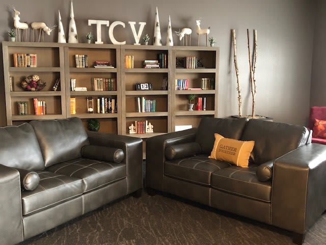 A cozy living room featuring two leather sofas, a bookshelf filled with books and decor, and a comfortable ambiance.