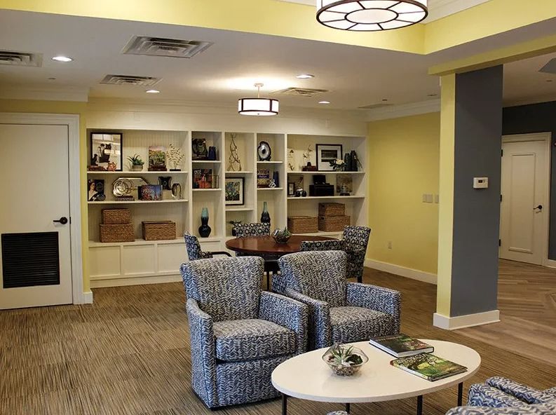 A cozy living room with armchairs, a round table, and bookshelves against a yellow wall.