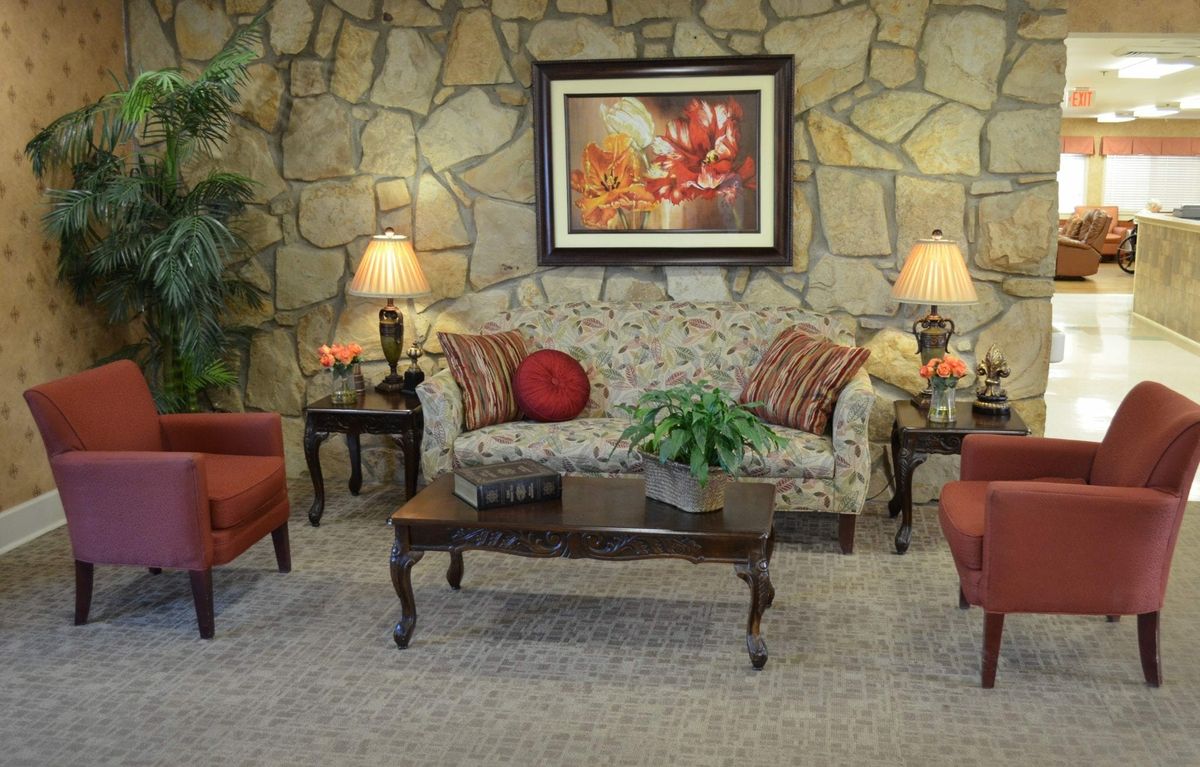 A cozy living room with a stone accent wall, featuring a floral sofa, red armchairs, a wooden coffee table, and decorative lamps.