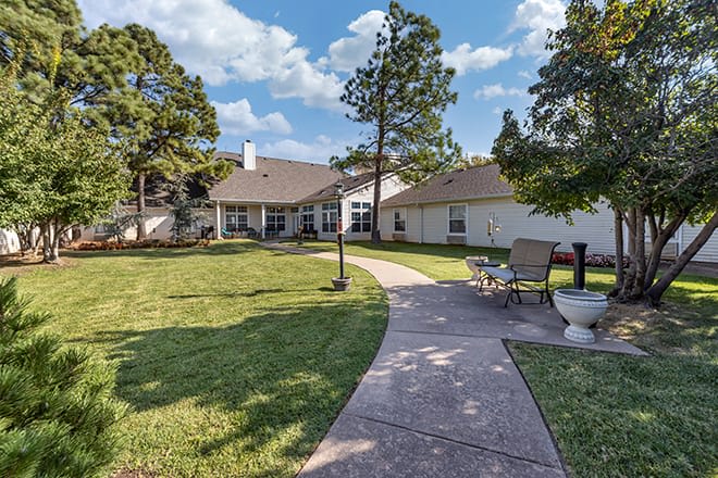 A spacious backyard with a pathway and outdoor furniture, surrounded by trees on a sunny day.