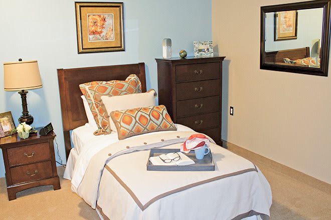 A cozy bedroom with a neatly made bed, decorative pillows, and a tray on the blanket.