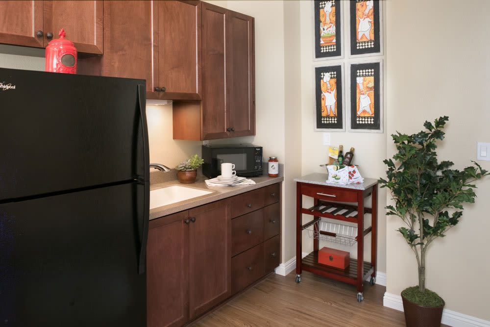 A cozy kitchen featuring dark wood cabinets, a black refrigerator, and a countertop with a sink and microwave.