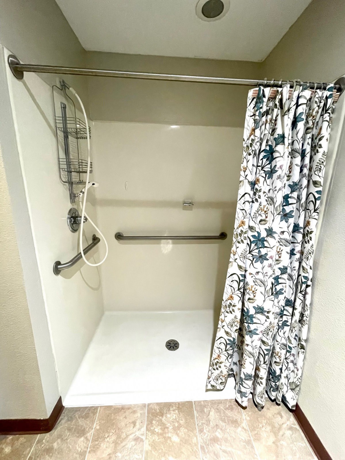 An accessible shower with grab bars, a handheld showerhead, and a floral patterned curtain.