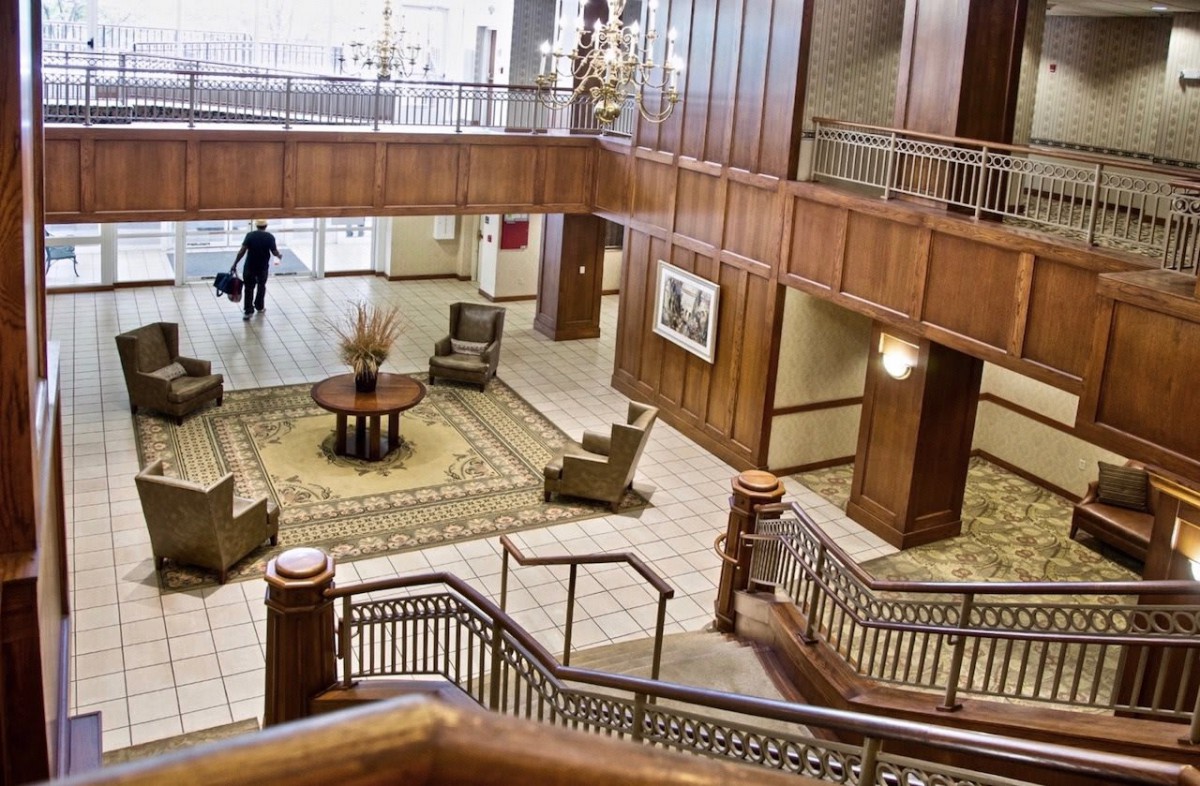 A spacious hotel lobby with elegant wood paneling, comfortable seating, and a grand staircase.