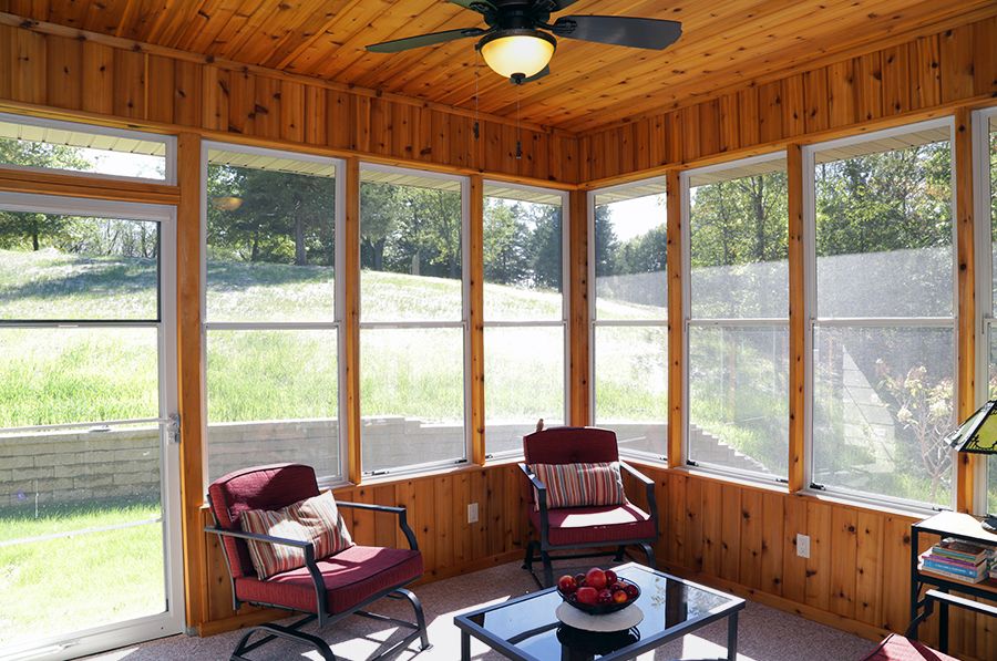 A cozy sunroom with wood paneling, featuring comfortable seating and abundant natural light.