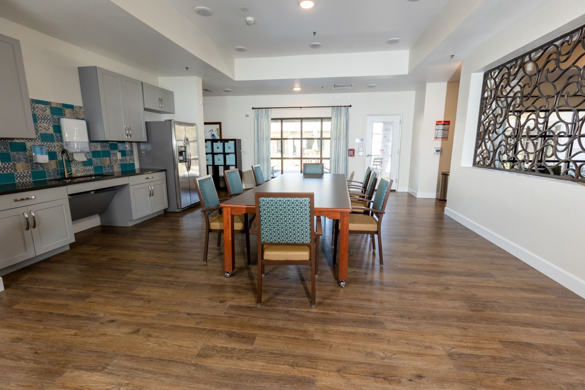 A spacious dining room with a large wooden table and chairs, featuring a modern kitchen area and wooden flooring.