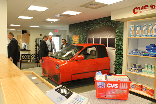 A red car on display inside a CVS store with people examining it.