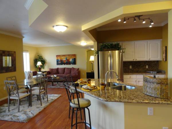A modern open-concept living space featuring a kitchen with granite countertops and bar stools, seamlessly integrated with a cozy living room.
