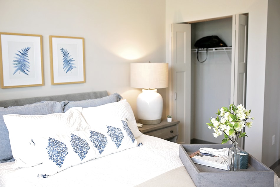 A cozy and minimalist bedroom with a bed, decorative pillows, a nightstand, and a lamp.