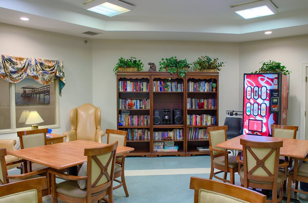 A cozy reading room with bookshelves, tables, and chairs, decorated with plants.