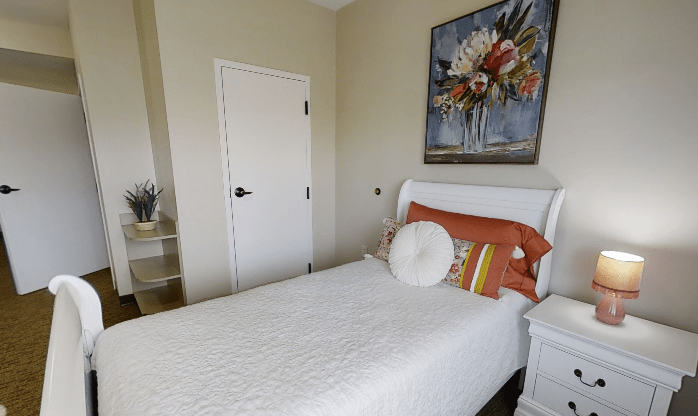 A cozy bedroom with a single bed, decorative pillows, and a floral painting on the wall.