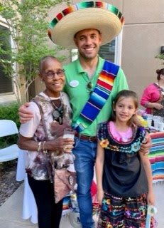 A group of three people smiling, dressed in festive and cultural attire outdoors.