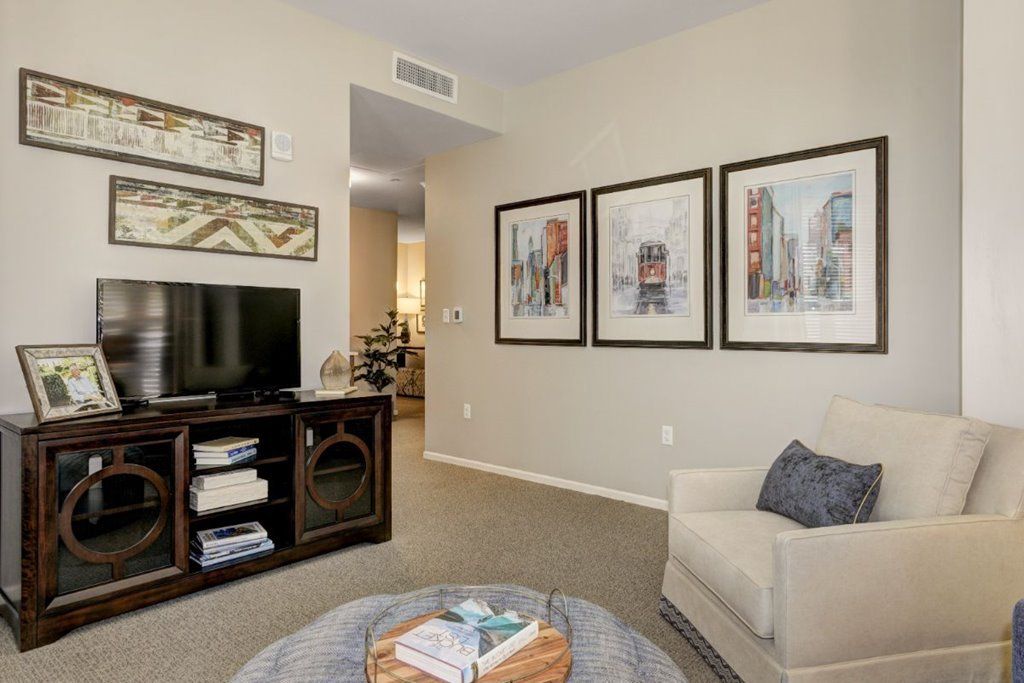 A cozy living room featuring modern decor, with framed artwork on the walls and a television on a wooden stand.
