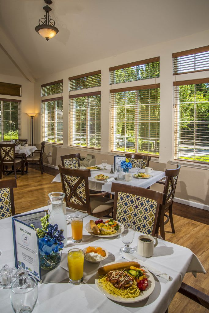 A cozy dining room with sunlit windows, set for a breakfast meal.