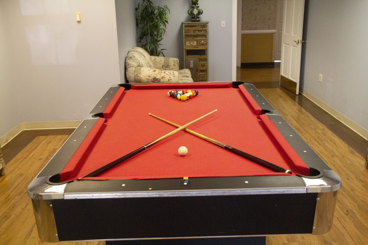 A red-felted pool table with crossed pool cues and a rack of billiard balls in a recreation room.