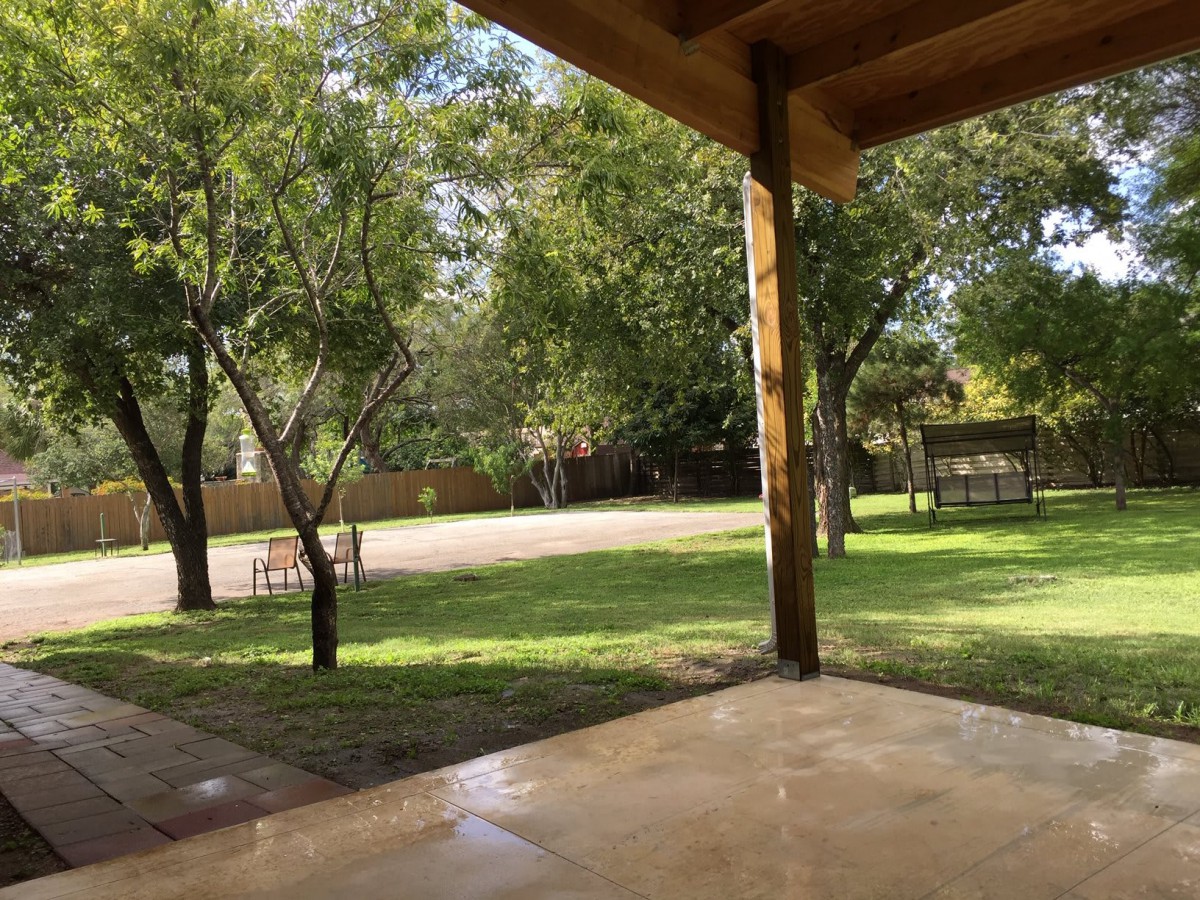 A view from a patio overlooking a lush yard with trees and sunlight.