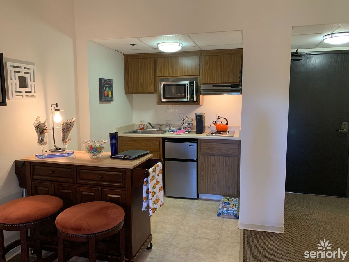 Compact apartment kitchen with wooden cabinets, microwave, and bar seating.