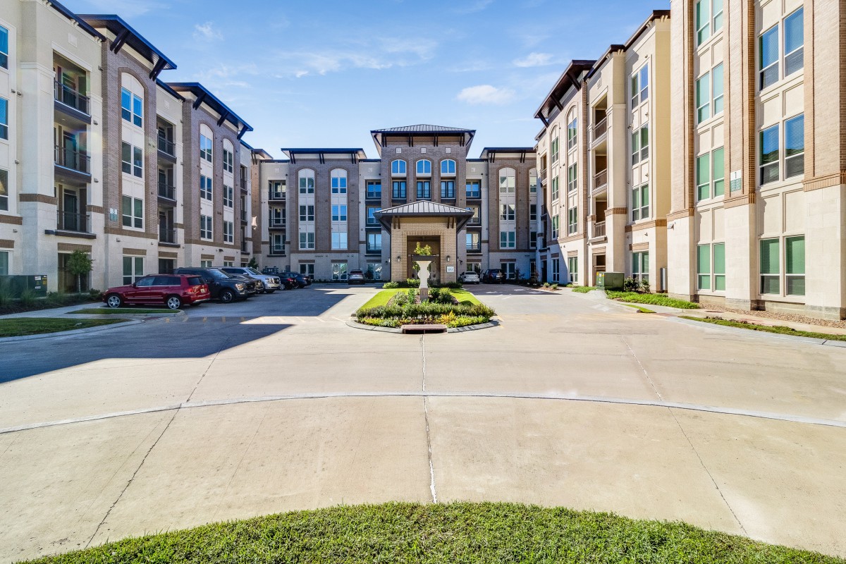 A modern apartment complex with a landscaped entrance and parking area.