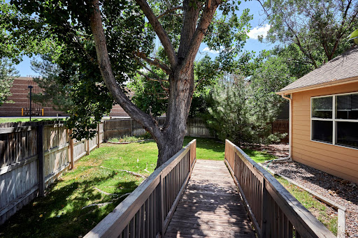 A serene view of a backyard featuring a wooden bridge leading through lush greenery and a mature tree.