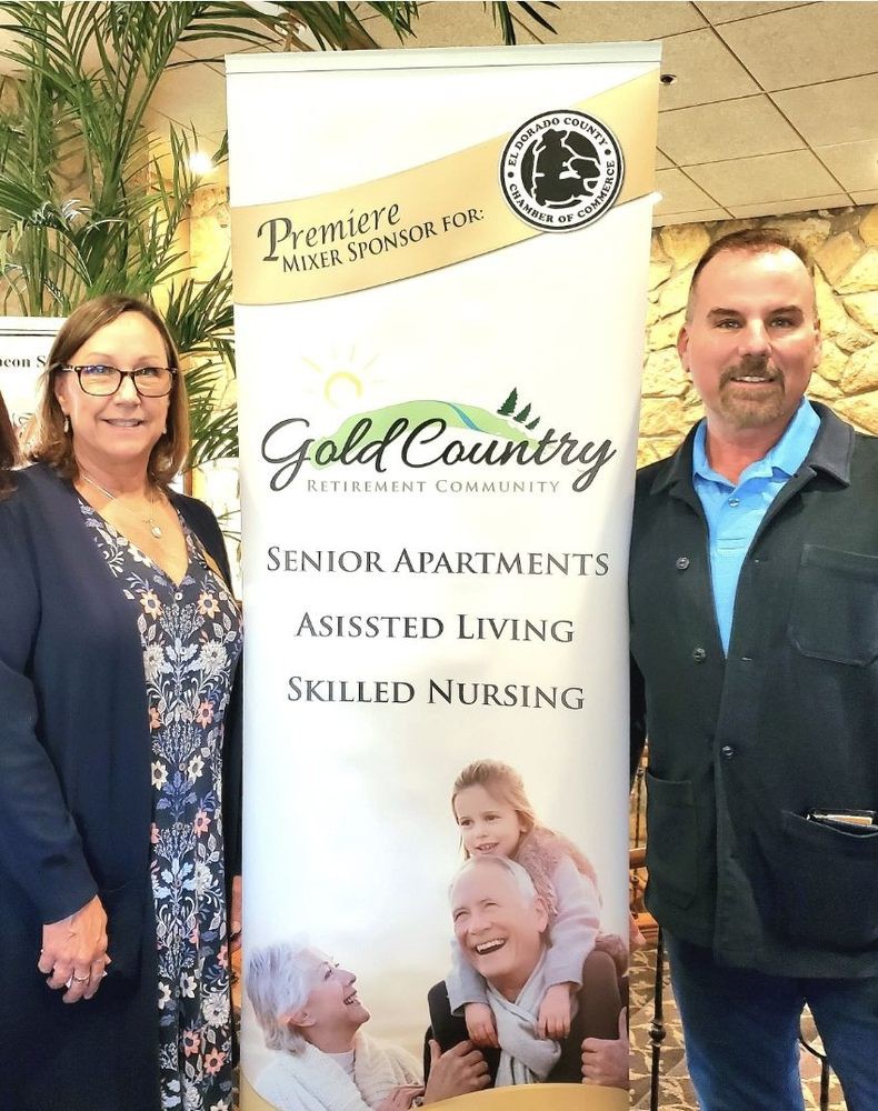 Two individuals standing next to a banner for Gold Country senior living services.