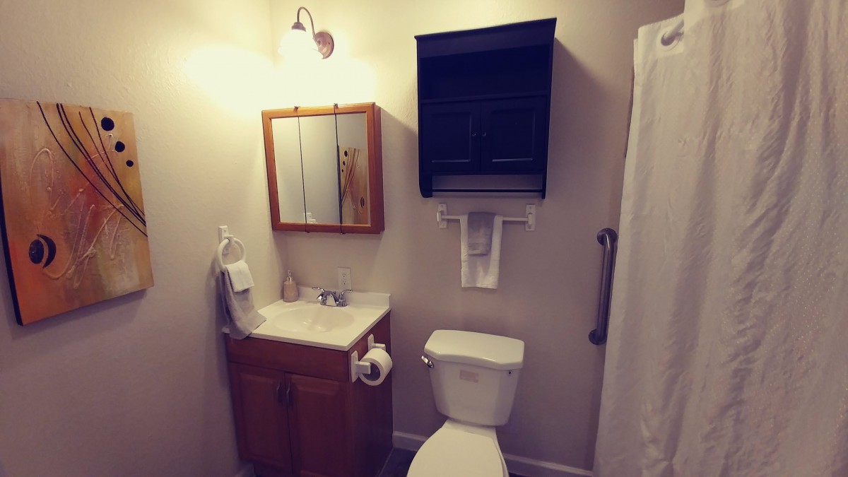A small, neatly organized bathroom with a sink, toilet, and mirror cabinet.