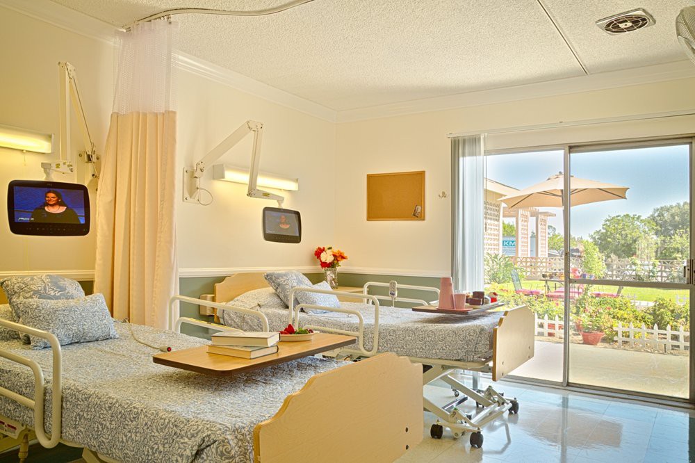 A well-lit hospital room featuring a patient bed and medical equipment, with a window offering an outdoor view.